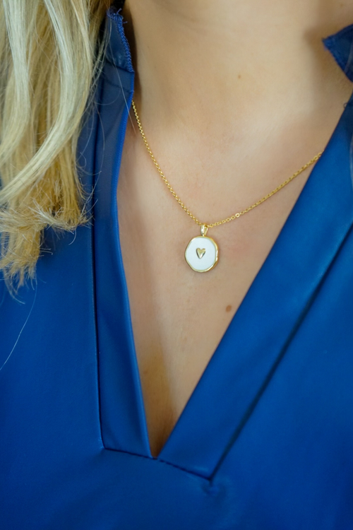 Dainty gold chain necklace with white enamel pendant with gold heart design.