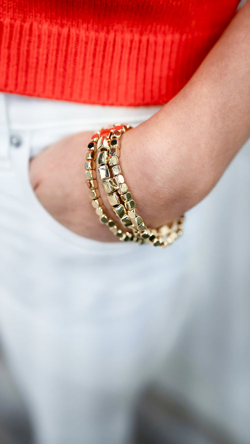 Model is wearing a gold square bead stack of three, stretch-design bracelets.