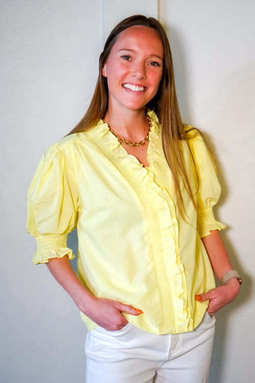 Model is wearing a yellow poplin blouse with short puff, ruffle sleeves with ruffle collar and placket.