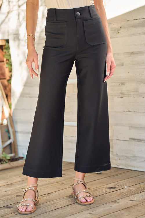 Model is wearing black front patch pocket pants made of comfortable stretch material.