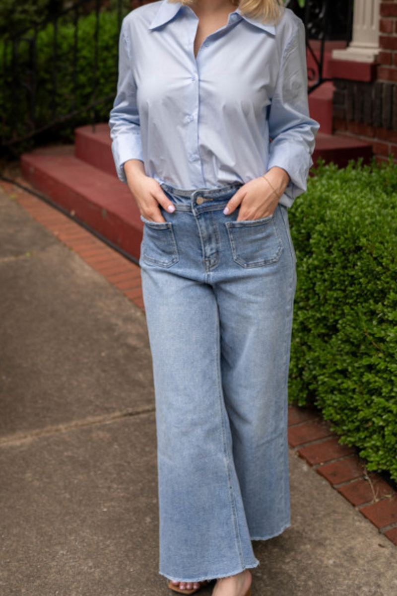 Model is wearing high-waisted cropped, full leg jeans by Mica that are fitted through the hips and have front and back patch pockets. They are a light wash to medium wash blue denim.