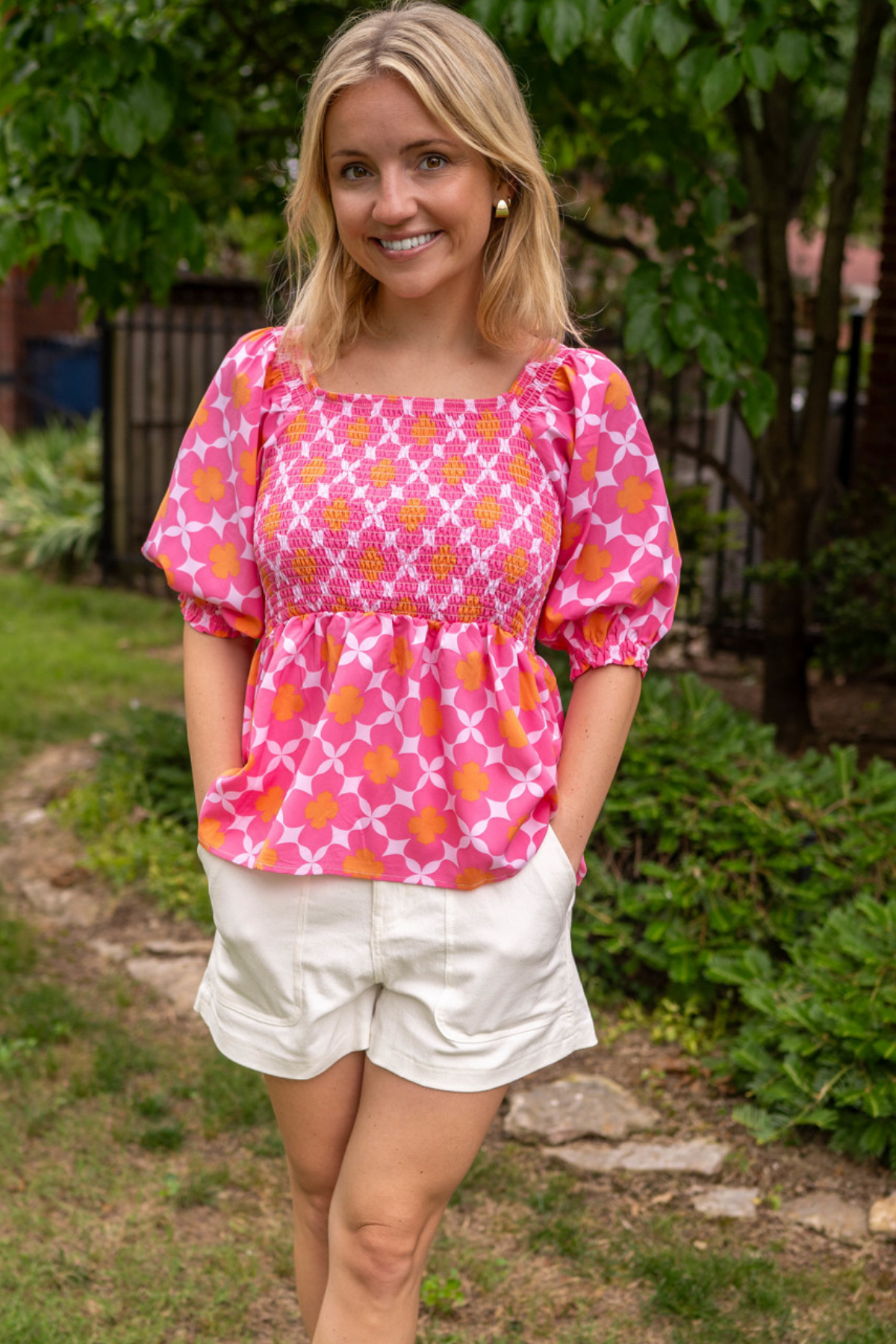 Model is wearing a babydoll design top with a peplum at the waist. It has a lightweight fabrication with pin, lilac and orange floral lattice design.