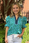 Model is wearing a blue and green ditsy print floral blouse with v-neck and puff sleeves.