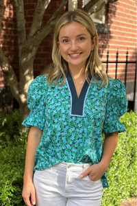 Model is wearing a blue and green ditsy print floral blouse with v-neck and puff sleeves.