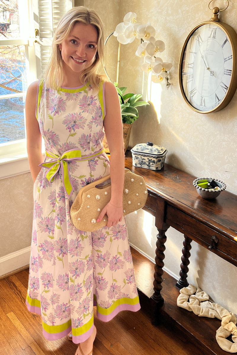 model is wearing a sleeveless midi dress with full skirt. It has a cream background with lilac and blue flowers.