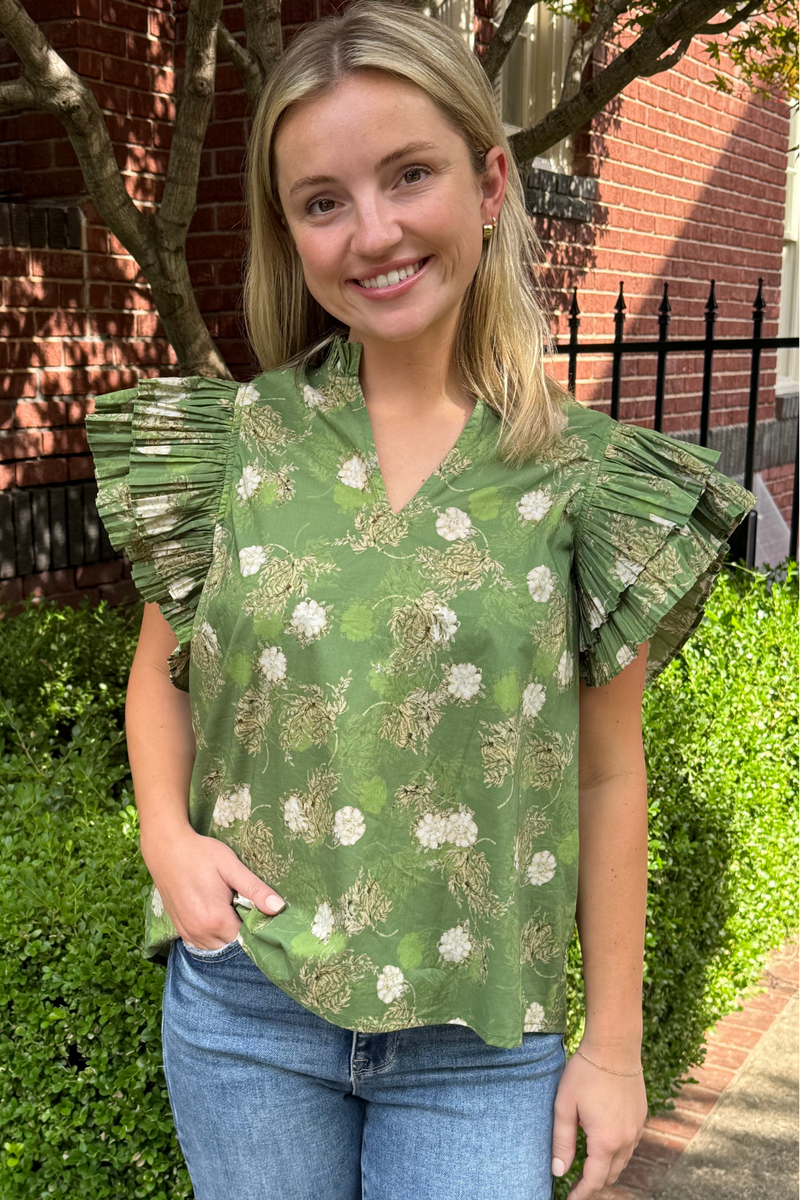 Model is wearing a v-neck, green short, double accordion ruffle top with cream botanical florals throughout.