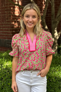 Model is wearing a green and pink ditsy floral top with short puff sleeves and v-neck design.