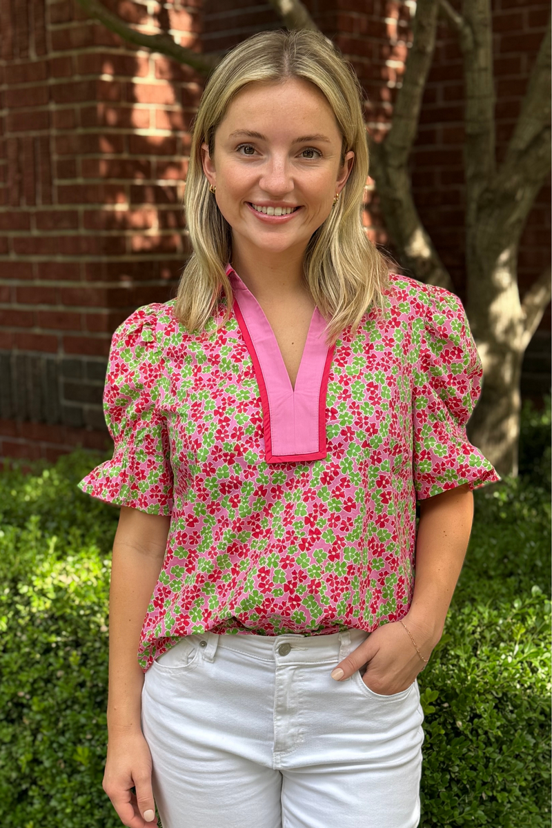 Model is wearing a green and pink ditsy floral top with short puff sleeves and v-neck design.