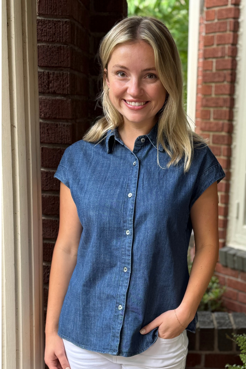 Model is wearing a dark wash denim button down shirt with cap sleeves.