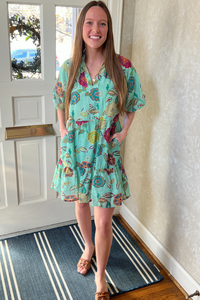 Model is wearing a green floral THML dress with v-neck, puff sleeves and ruffle skirt.