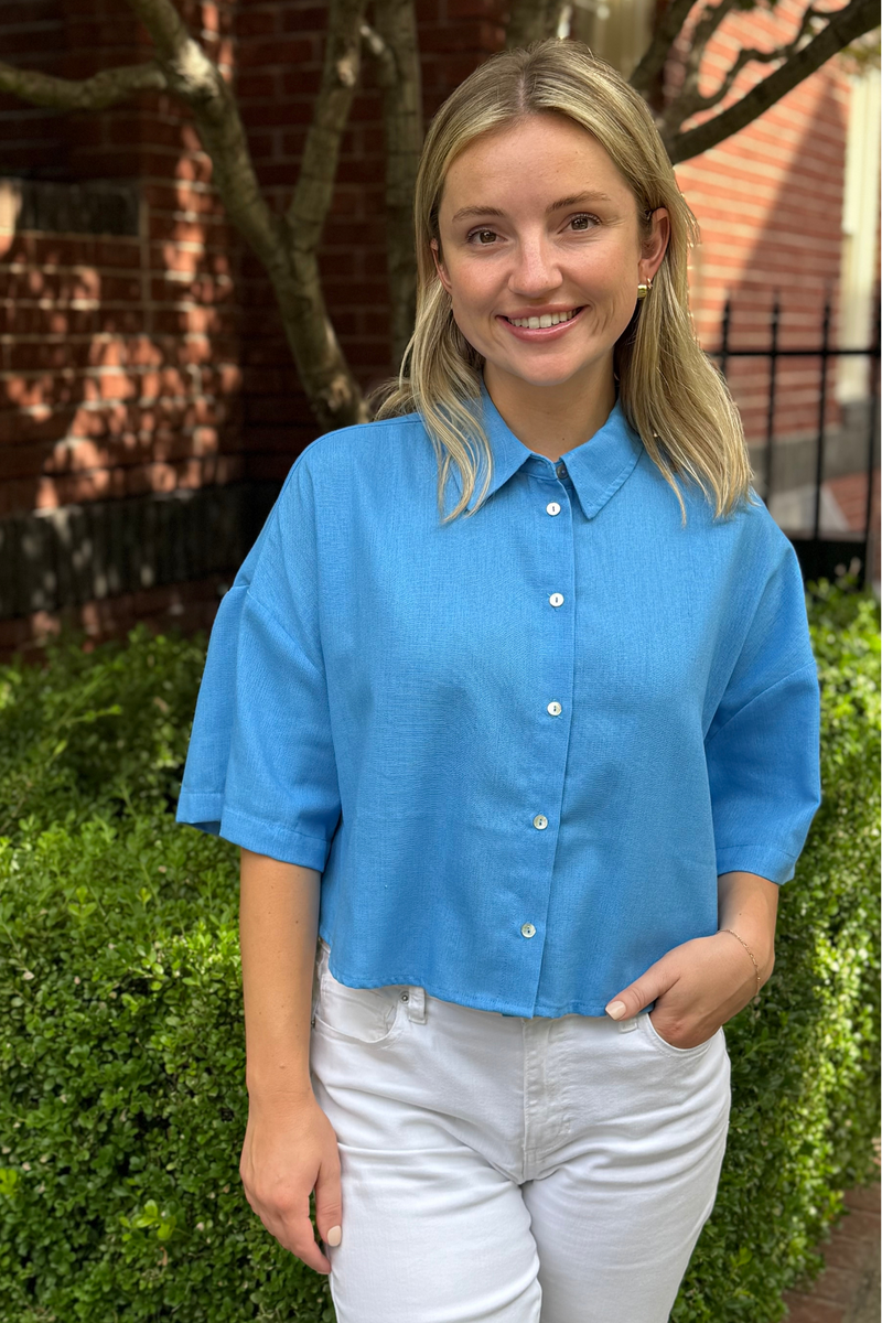 Model is wearing an azure blue boxy, short sleeve, button down shirt.