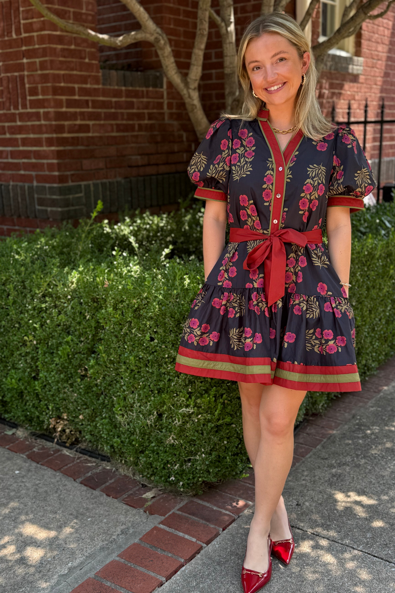 Model is wearing a black, wine and olive floral dress with drop ruffle skirt and puff sleeves.