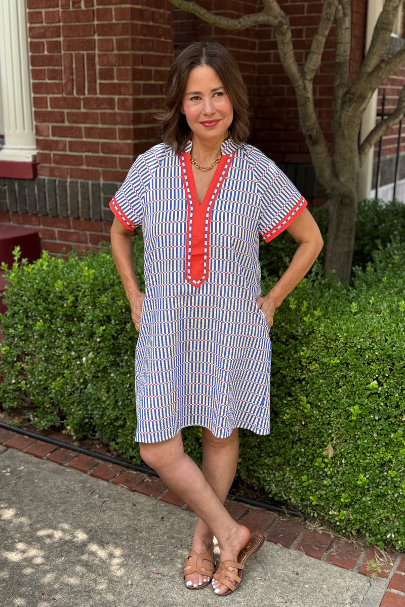 Model is wearing a blue and white, short sleeved, striped dress with orange trim along the v-neck bodice and sleeves
