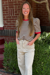 Model is wearing a cream puff sleeve top with chocolate brown stripes and red banding around the neck and arms.
