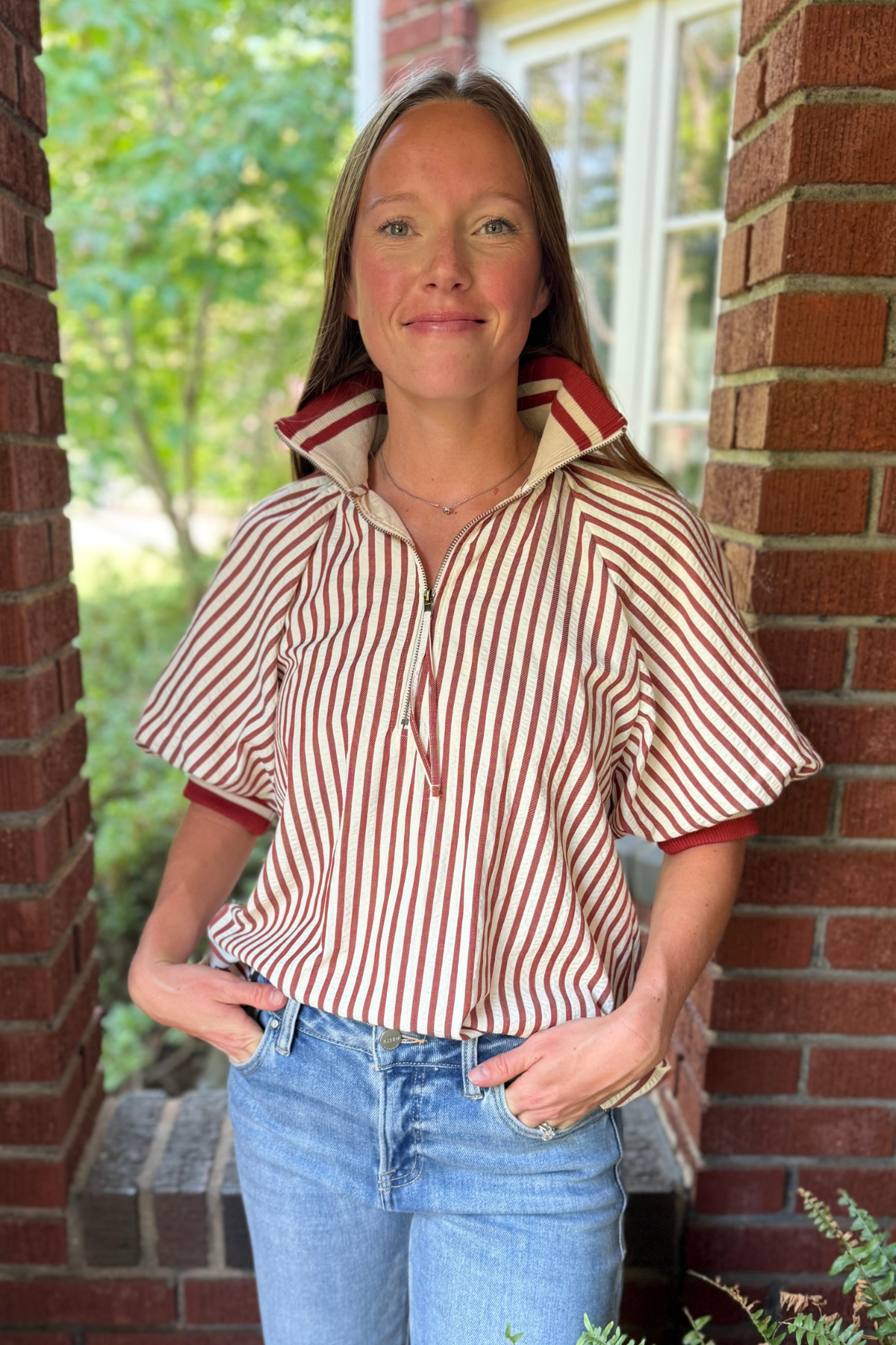 Model is wearing a crimson and cream seer sucker striped top with zipper collar.
