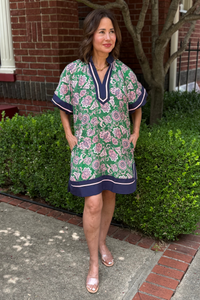 Model is wearing a straight green and pink floral dress with navy and pink trim along the hem, sleeves and v-neckline.