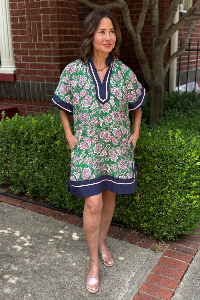 Model is wearing a straight green and pink floral dress with navy and pink trim along the hem, sleeves and v-neckline.