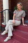 Model is wearing a ecru leopard print sweater with red banding around the sleeves, waist and neck. It has short puff sleeves.