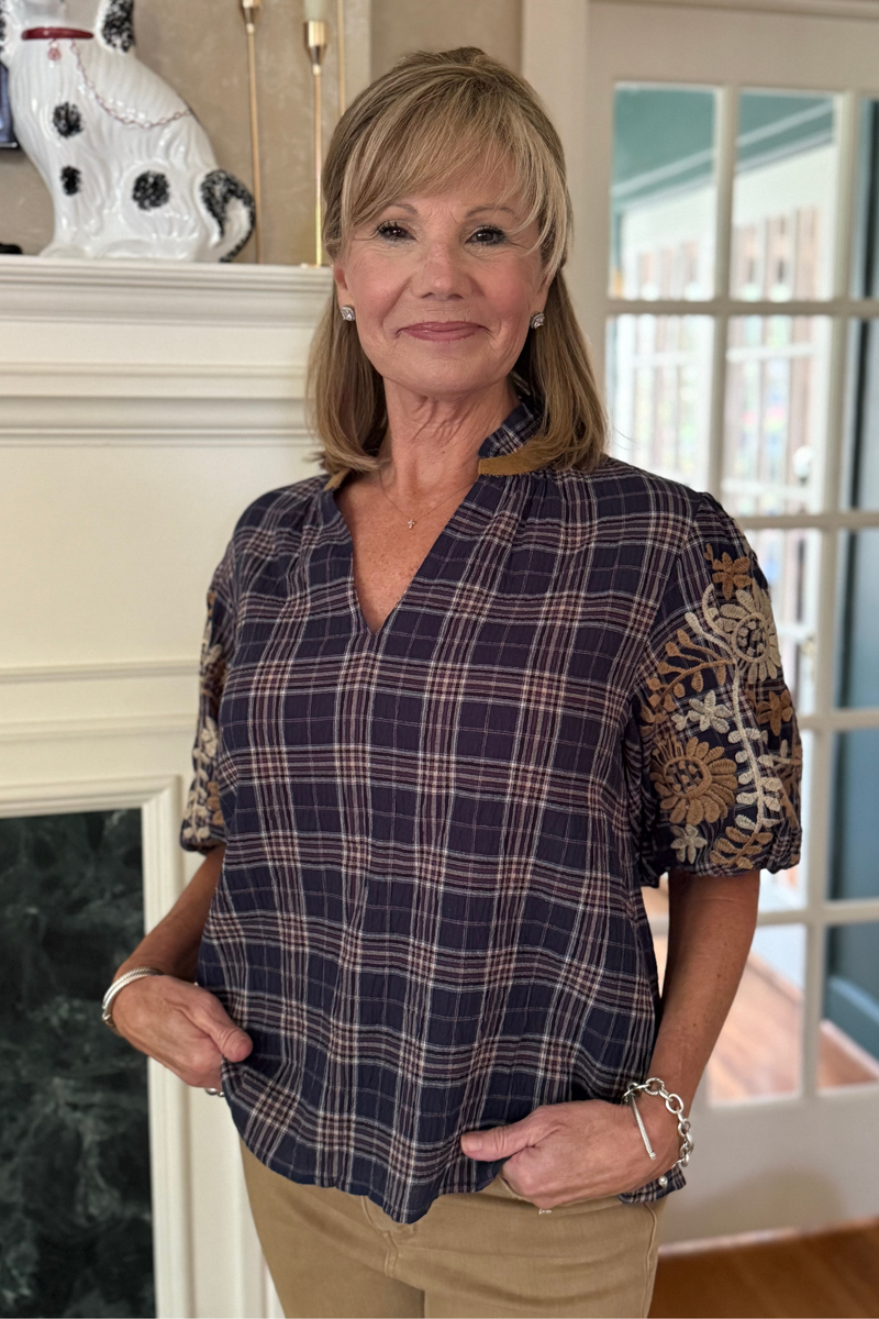 Model is wearing a navy, cream and camel plaid top with embroidered puff sleeves.