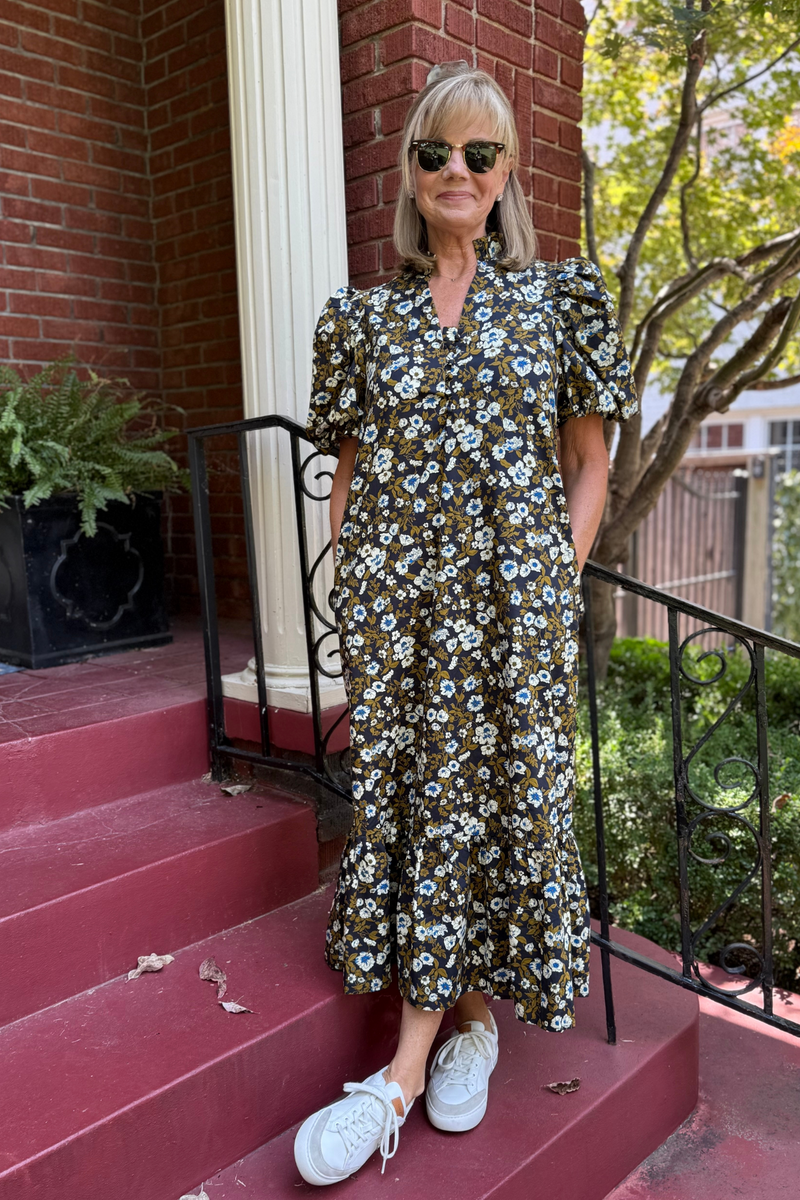 Model is wearing a chocolate, cream and blue floral dress with v-neck, puff sleeves and a tiered midi skirt.