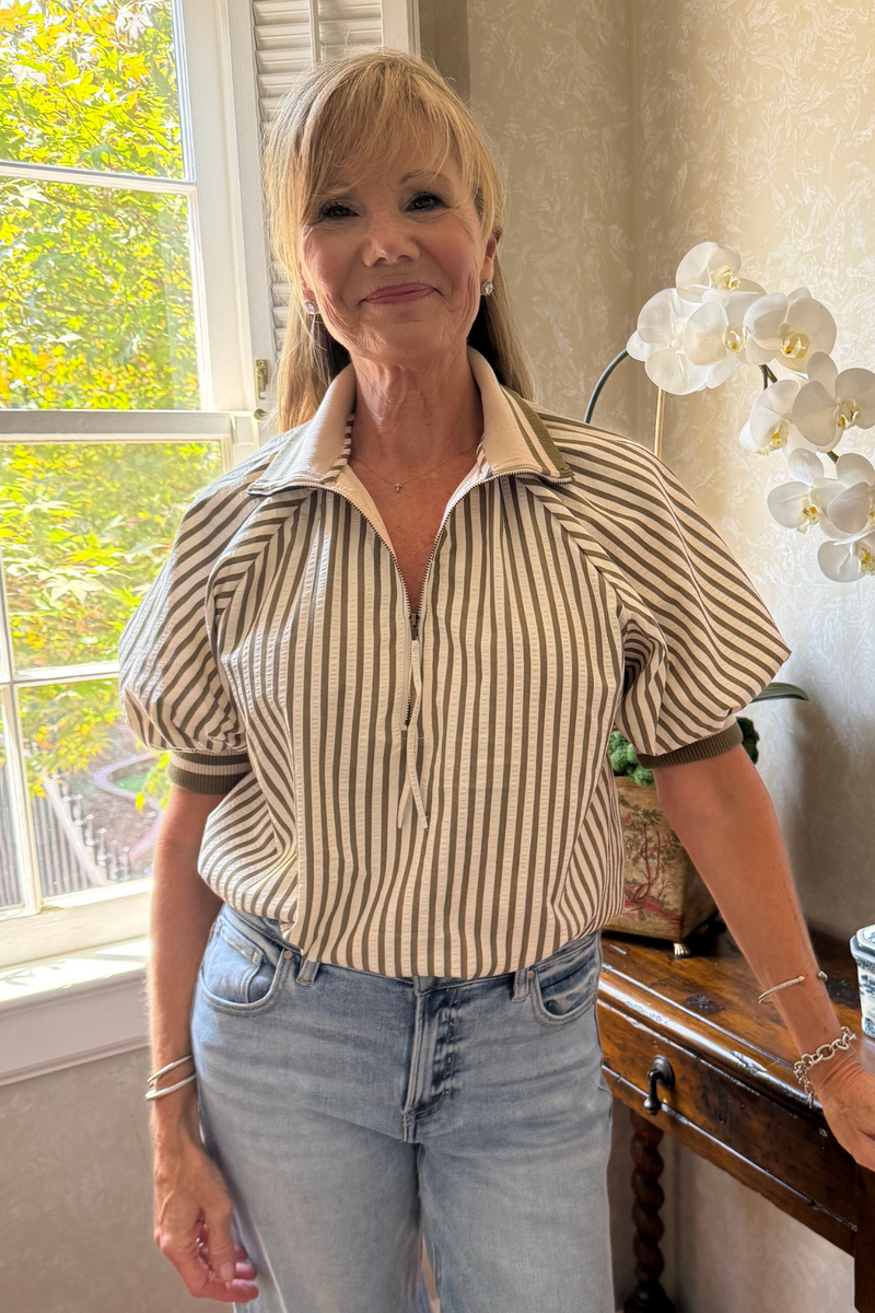 Model is wearing an olive and cream striped top with zipper collar detail and puff sleeves.