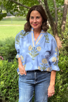 Model is wearing a periwinkle blue shirt with blue and yellow tape detail along the v-neckline and yellow and green botanical pattern throughout.
