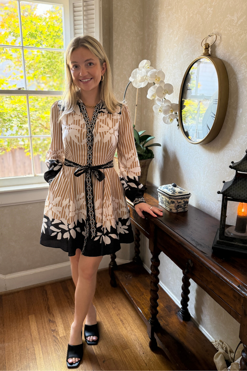 Model is wearing a camel and ecru striped dress with ecru floral design detail.