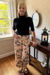 Model is wearing a high-rise, full-leg cotton twill pant in beige with a brown and black floral motif.