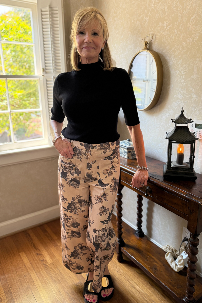 Model is wearing a high-rise, full-leg cotton twill pant in beige with a brown and black floral motif.