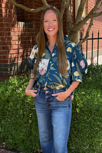Model is wearing a teal botanical short sleeve button down shirt.