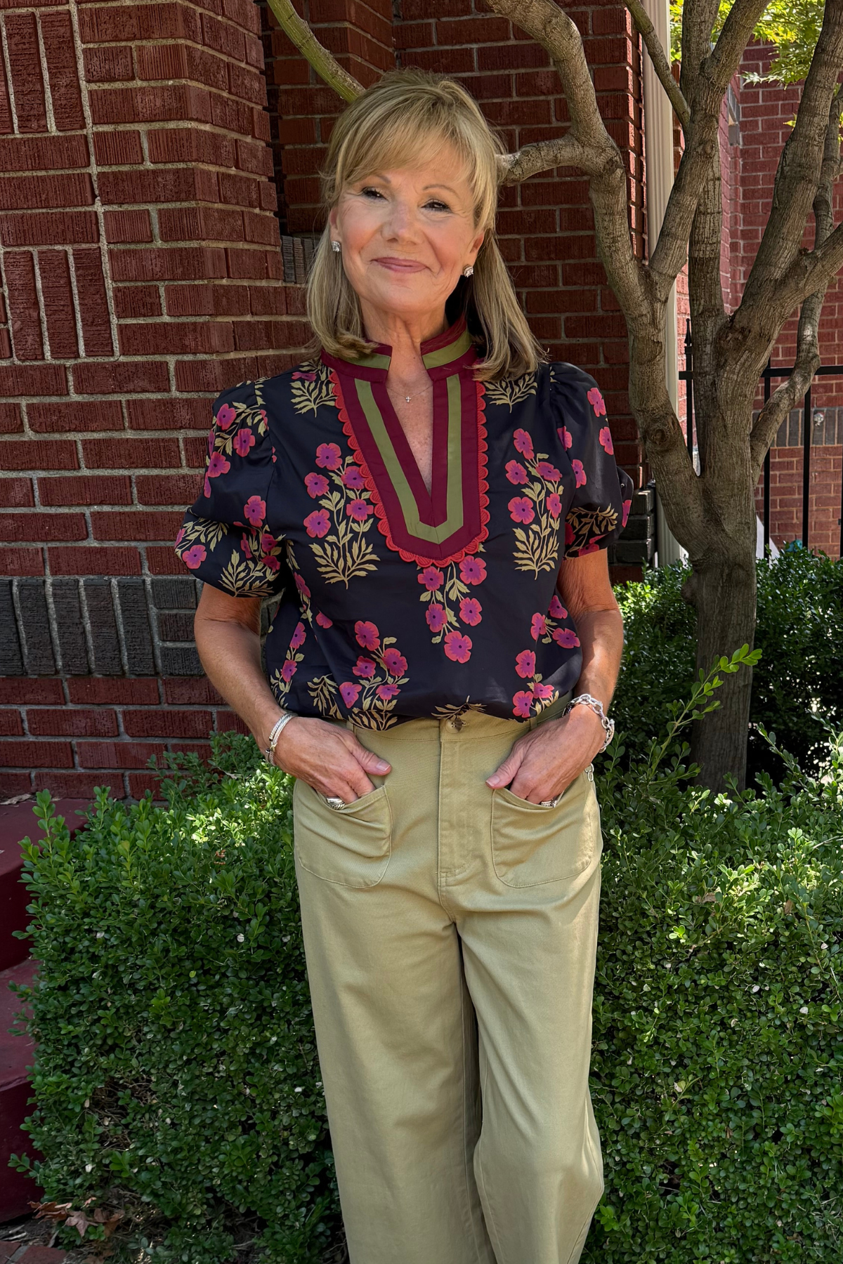 Model is wearing a black blouse with pink, olive and burgundy floral print. 