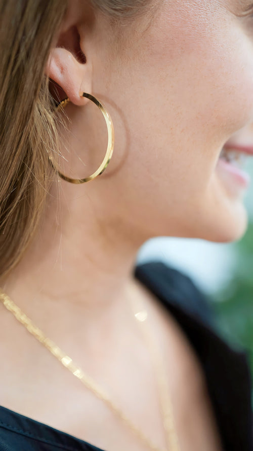 Model is wearing flat gold hoop earrings