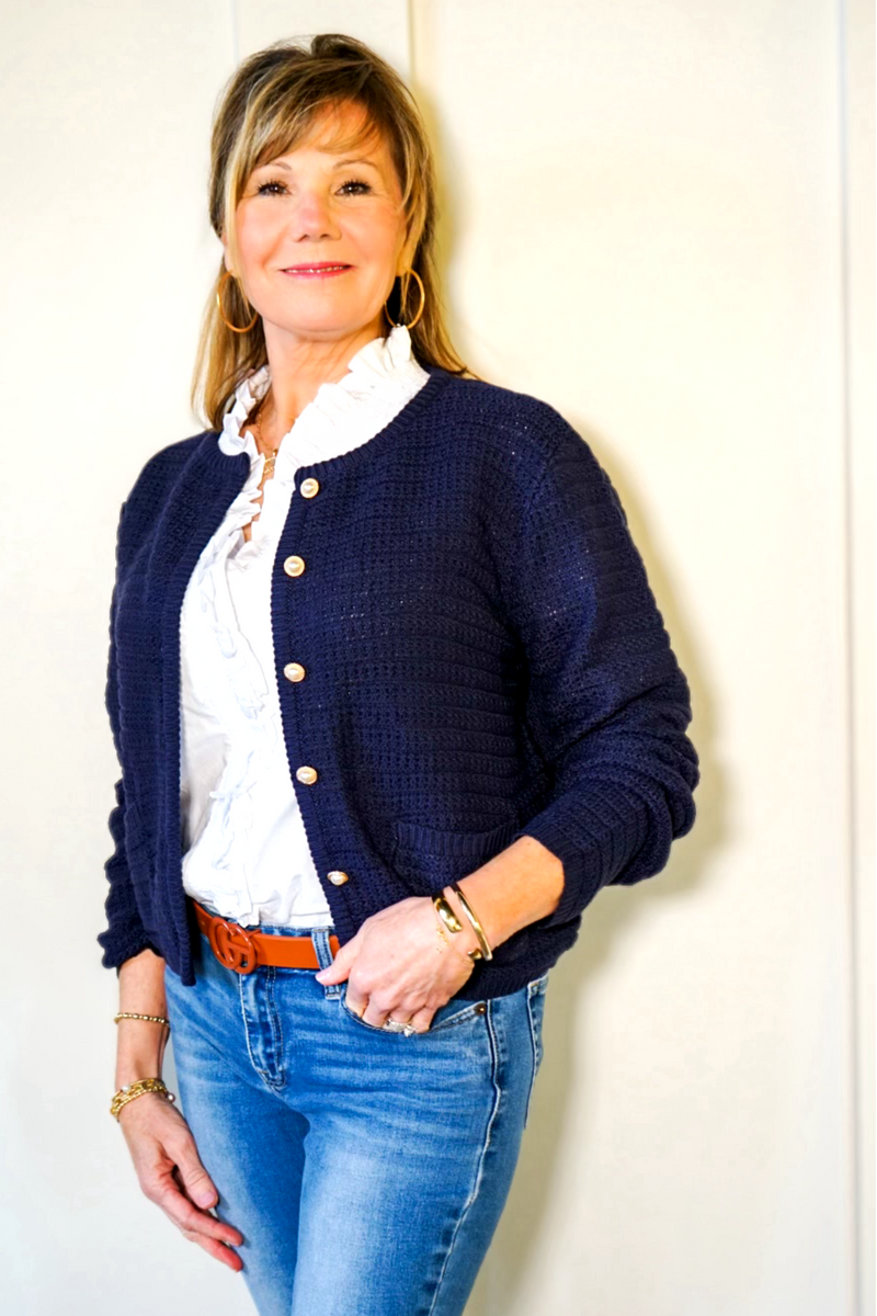 Model is wearing a navy light weight, long-sleeved cardigan with pearl buttons and front patch pockets