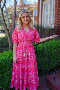 Model is wearing a pink, magenta and lilac V-neck midi dress with empire waist and flowy ruffle skirt.