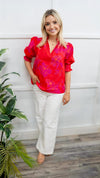 Model is wearing a puff sleeve, poplin blouse in red and magenta.