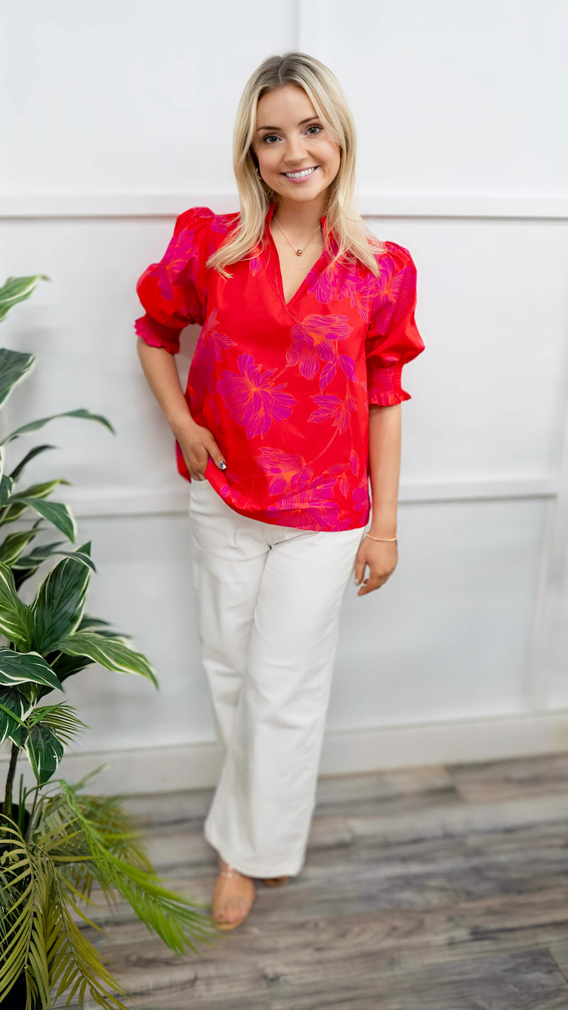 Model is wearing a puff sleeve, poplin blouse in red and magenta.