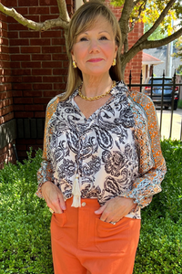 Model is wearing  silk ivory and black paisley print blouse with self tie.