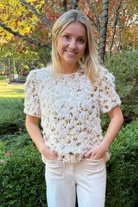 Model is wearing a cream shag-type fabrication top with large gold sequins by THML.