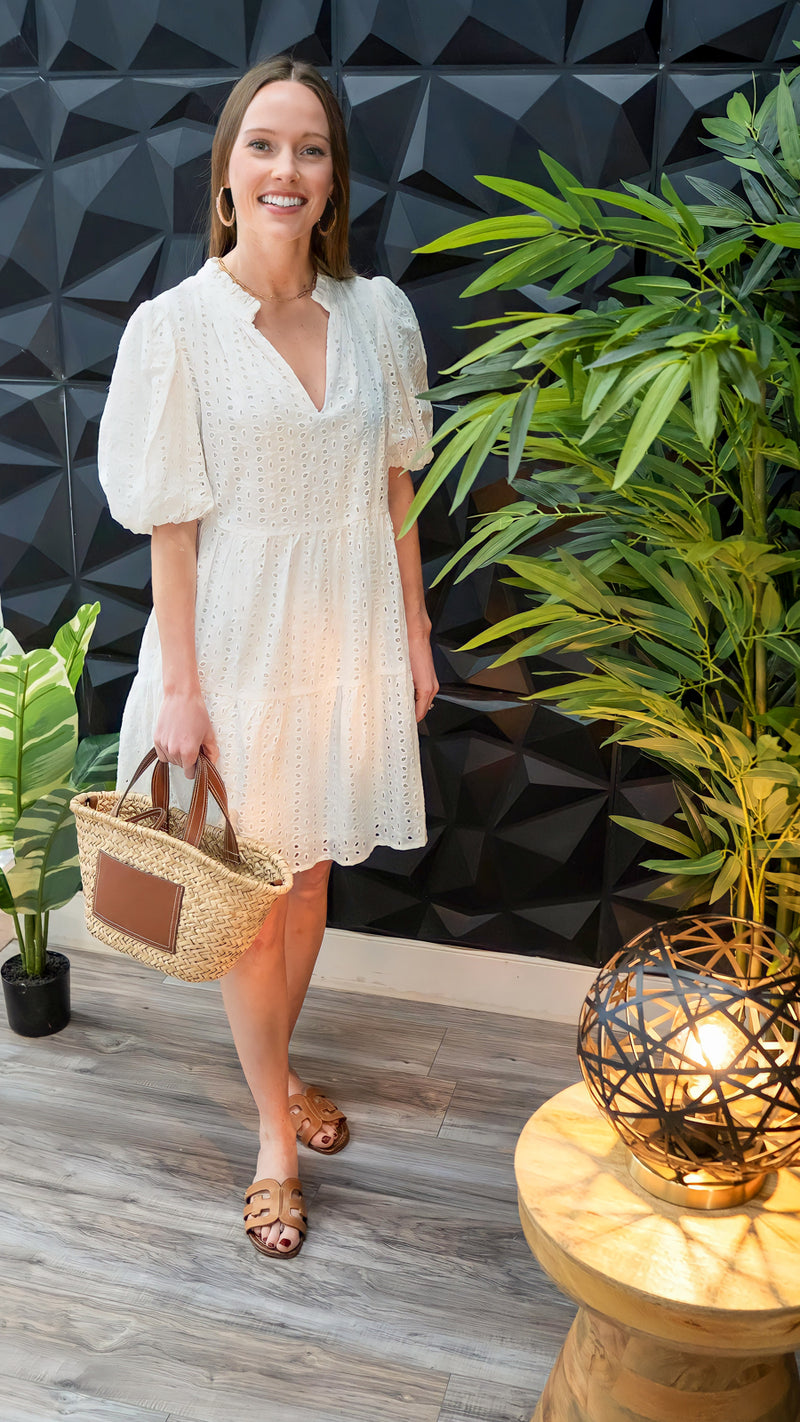 Model is wearing a white eyelet dress with v-neck and puff sleeves