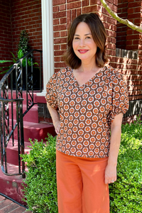 Model is wearing a v-neck, puff sleeve cotton top with chocolate, ecru and rust floral pattern throughout.