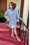 Model is wearing a medium wash denim dress with rolled tab sleeves and flattering collard, v-neck design