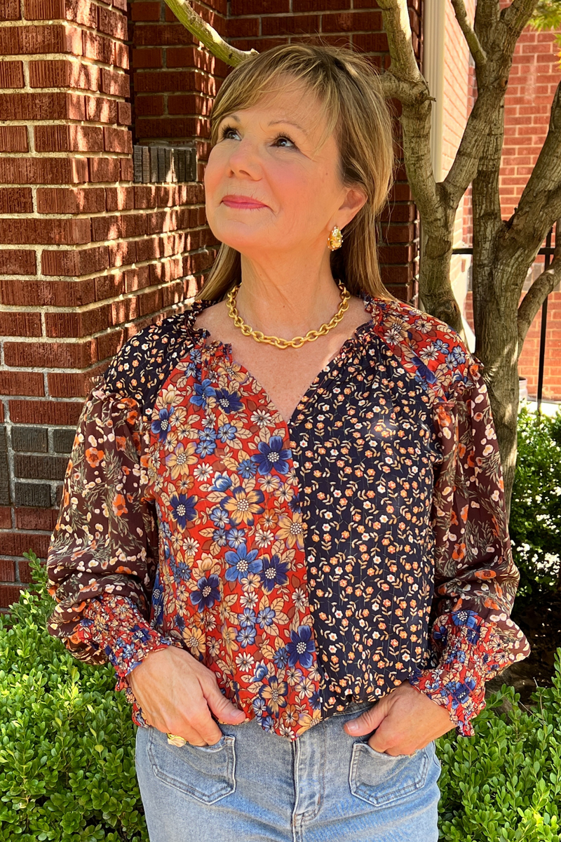 Model is wearing a long sleeved ditsy print top with ve neckline, ruched and ruffles at the wrists and peasant design.