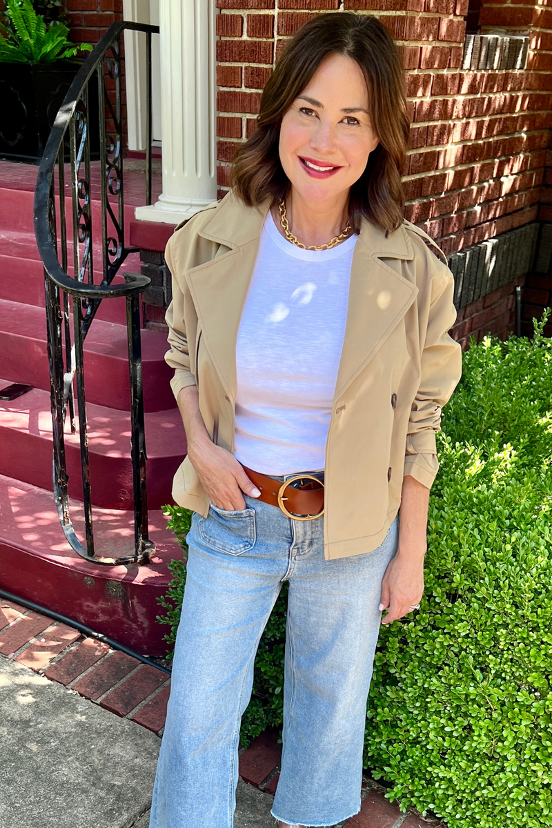 Model is wearing a camel colored cropped trench coat with cuff detail.