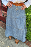 Model is wearing a medium wash, tiered denim maxi skirt with silver exposed buttons on the front and elasticized waistband on back.