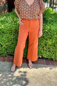 Model is wearing terra cotta colored cropped, wide leg twill pants with front and back patch pockets.