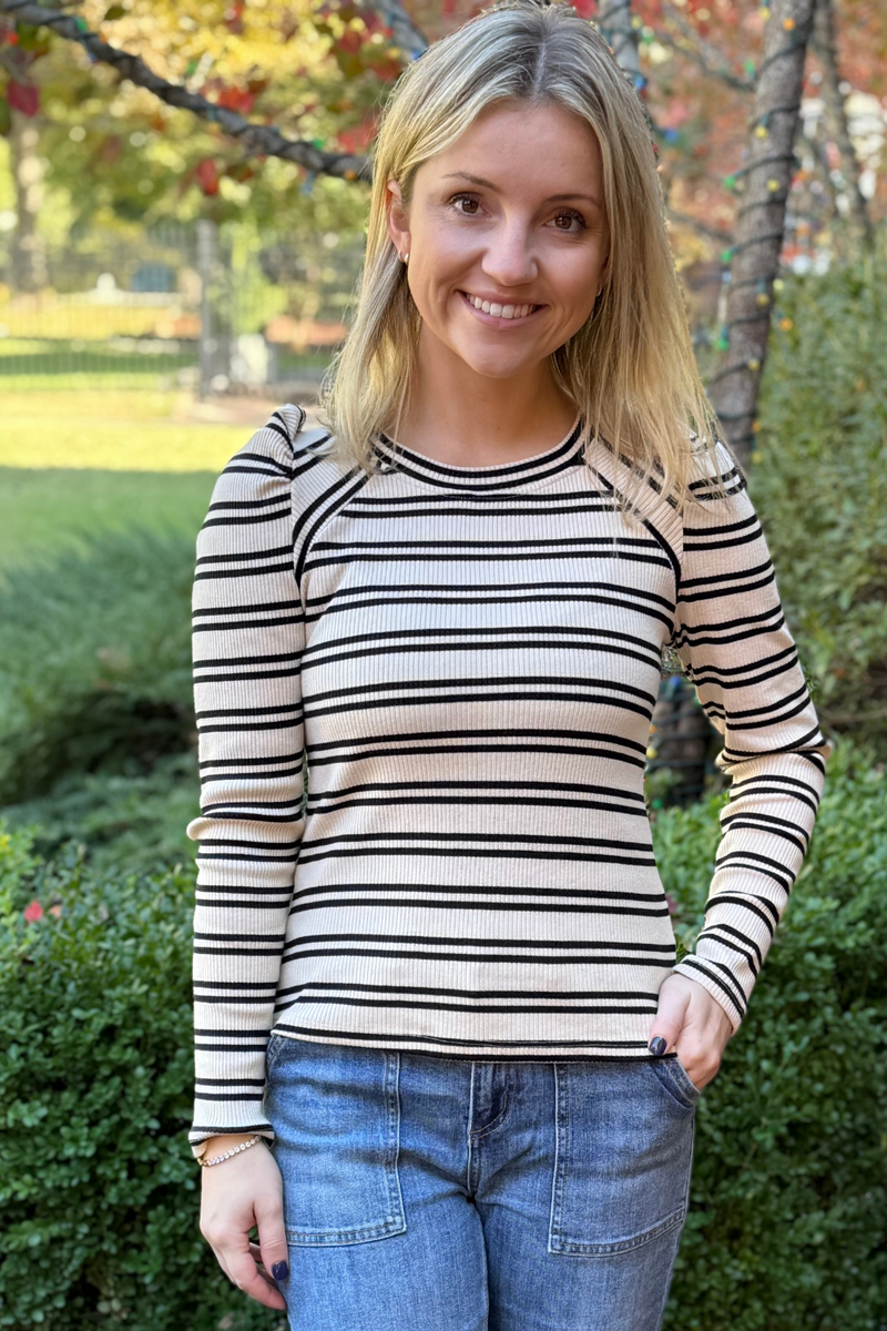 model is wearing a long sleeved, cream knit top with black stripes and slight puff sleeves.