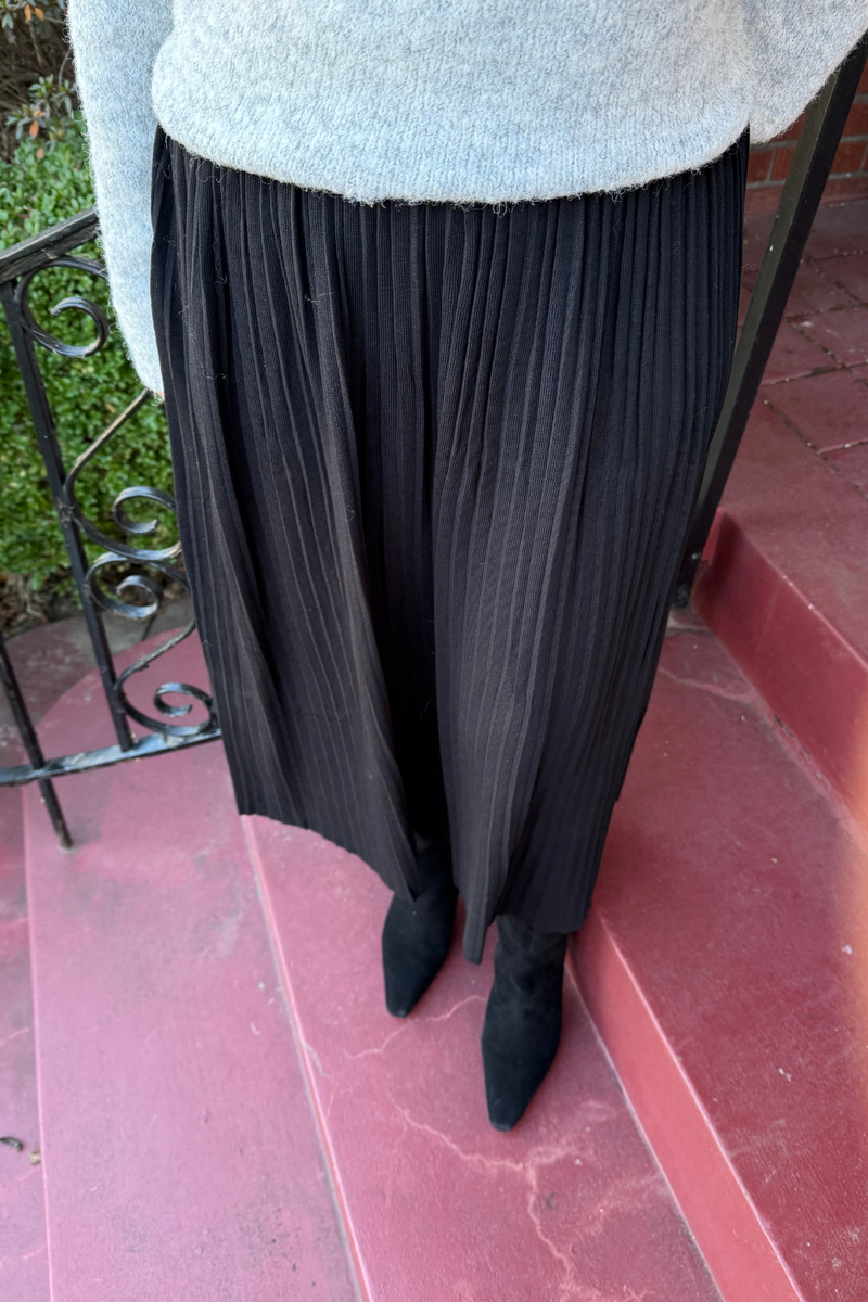 model is wearing a black knit pleated skirt with elasticized waist band.