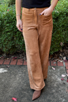 model is wearing caramel colored faux suede pants with full leg, tortoise  button closure and patch pockets in front and back.