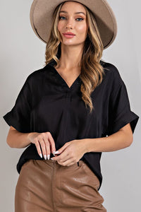 Model is wearing a relaxed fit black popover silky blouse with collared v-neck and rolled short sleeves.